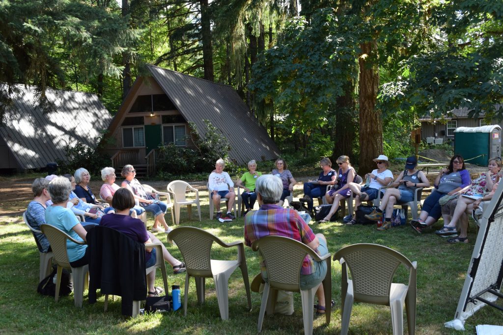 Twenty-five women sitting in a circle of chairs in from of the a-frame cabins during Women's Weekend at Camp Lutherwood Oregon